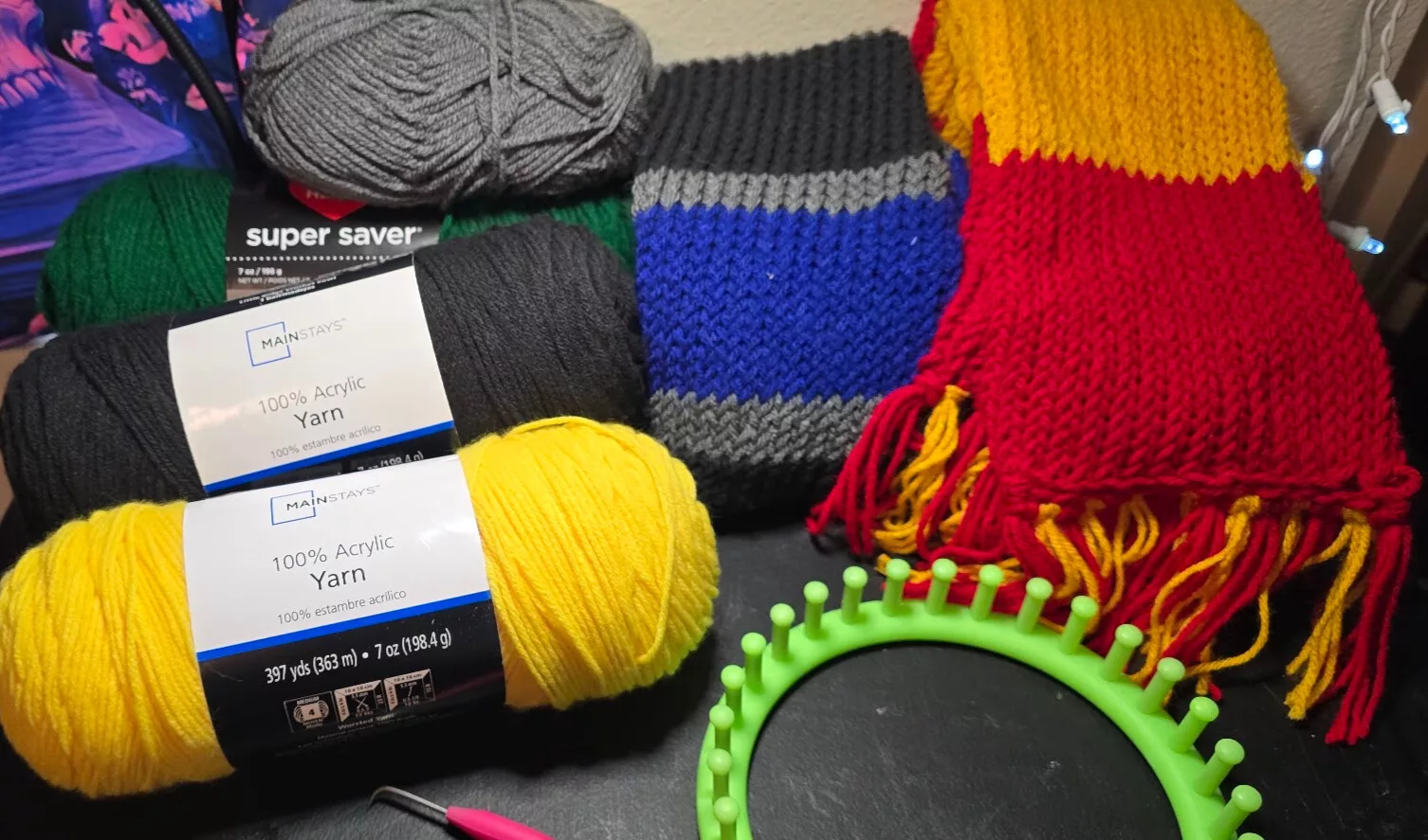 Yarn, loom, and finished scarves used to create loom knit scarf patterns in red, yellow, blue, and green.