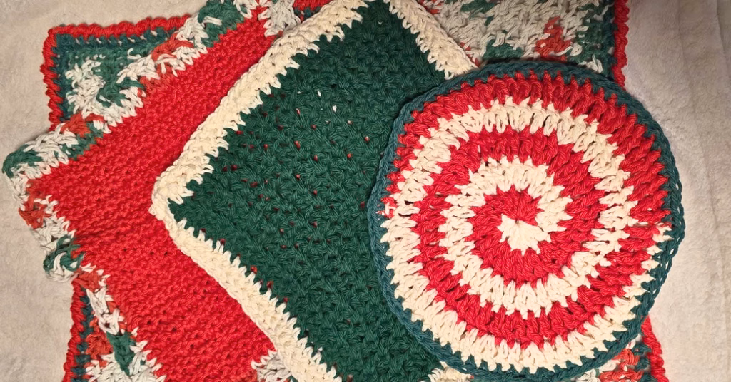 Christmas crochet kitchen set featuring four handmade pieces in festive red, green, and cream cotton yarn, including two textured dishcloths, a towel, and a peppermint spiral trivet.
