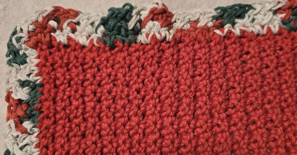 Cranberry textured crochet dishcloth with a Christmas-variegated crossed half double crochet border, part of a handmade Christmas crochet kitchen set.