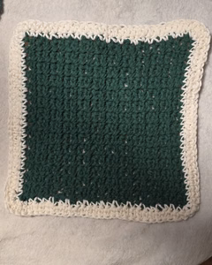 Evergreen moss stitch dishcloth with an ivory herringbone border laid flat, part of a handmade Christmas crochet kitchen set.