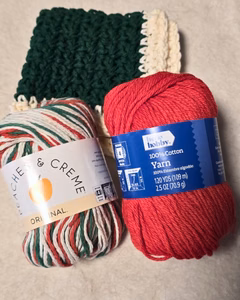 Christmas crochet kitchen set materials featuring skeins of cotton yarn in red, green, ecru, and yuletide